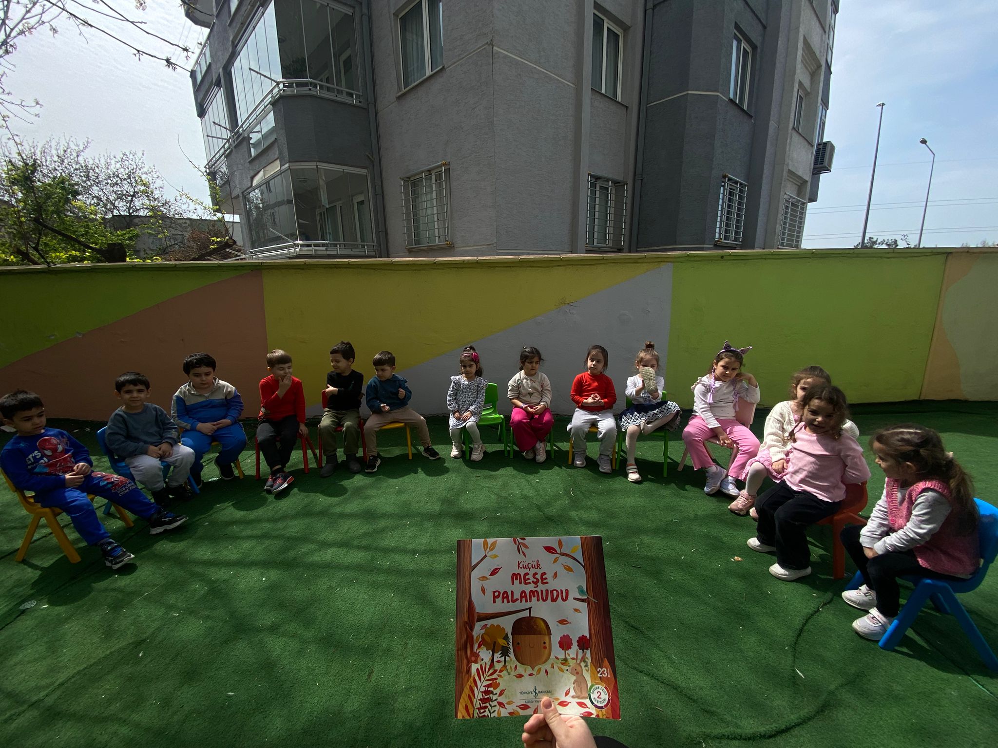 Bahçede kitap etkinliği için halka olan çocuklar